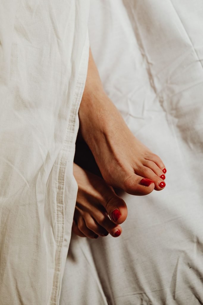 15 Winter Pedicure Colors You Need to Try in 2026 (With Exact Shade Names) classic red winter pedicure on cozy white bedding